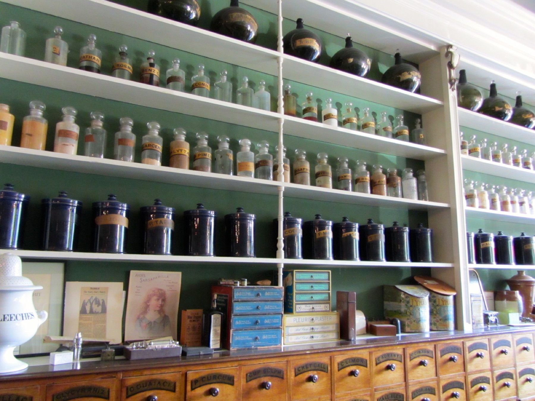 Shelves of an old apothecary lined with labeled glass bottles, dark jars and wooden drawers
