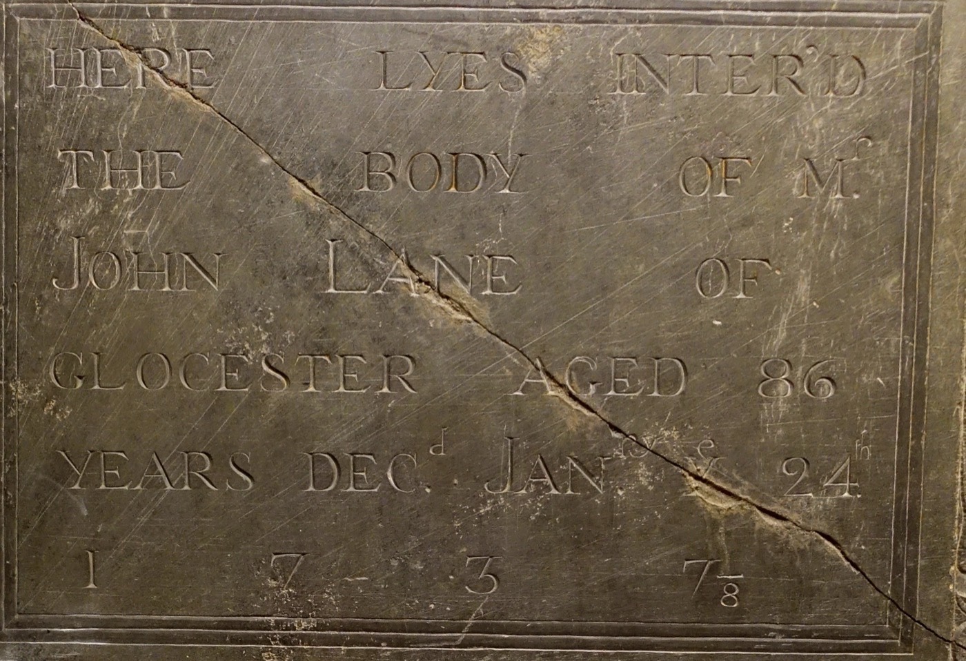Slate gravestone inscription in capital letters, cracked diagonally, ending with the year 1737 with a small 8 written under the final 7